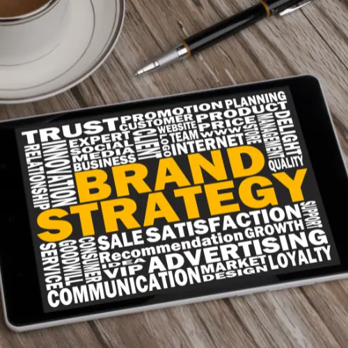 Tablet on table with coffee and pen with Brand Strategy in Yellow with words related around in White